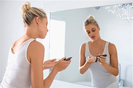 Beautiful young woman applying moisturizer on her face in bathroom Foto de stock - Sin royalties Premium, Código: 6108-08662423