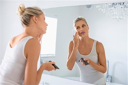 Beautiful young woman applying moisturizer on her face in bathroom Stock Photo - Premium Royalty-Free, Code: 6108-08662422