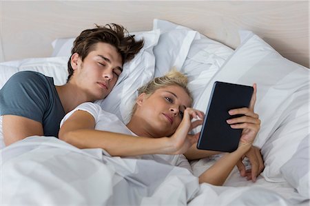 Young woman using a digital tablet with her boyfriend sleeping near her Stock Photo - Premium Royalty-Free, Code: 6108-08662538