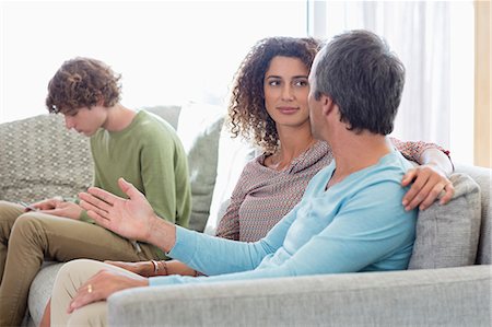 son and dad talking by cell phone - Happy family sitting in a living room at home Stock Photo - Premium Royalty-Free, Code: 6108-08662770