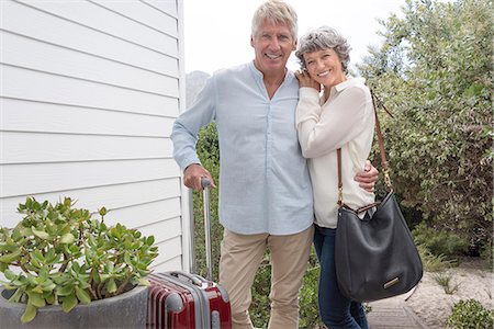 Happy senior couple standing with suitcase outside of house Stock Photo - Premium Royalty-Free, Code: 6108-08662734