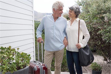 Happy senior couple standing with suitcase outside of house Stock Photo - Premium Royalty-Free, Code: 6108-08662735