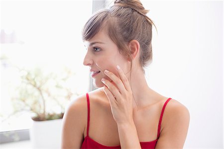 simsearch:6108-07969480,k - Beautiful woman applying moisturizer on face in bathroom Foto de stock - Sin royalties Premium, Código: 6108-08662833