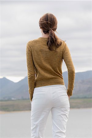 Rear view of a woman standing at lakeshore looking at view Stock Photo - Premium Royalty-Free, Code: 6108-08662927