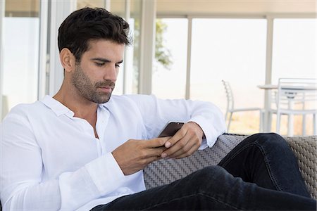 Man using a mobile phone at home Foto de stock - Sin royalties Premium, Código: 6108-08663221