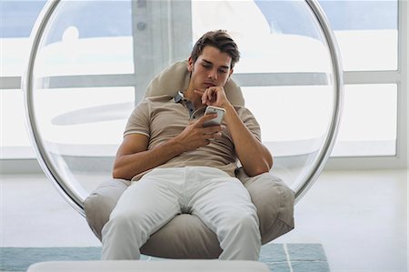 Man sitting in a chair using a smart phone Stock Photo - Premium Royalty-Free, Code: 6108-08663374