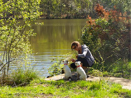 Young woman sitting with her dogs by a lake Stock Photo - Premium Royalty-Free, Code: 6108-08636802