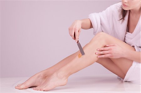 simsearch:6108-08637305,k - Young woman applying wax on her legs Stock Photo - Premium Royalty-Free, Code: 6108-08637306