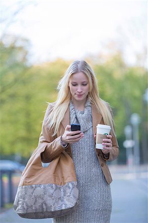 simsearch:6108-08943497,k - Pretty blonde woman checking her mobile with coffee to go walking in city center Stock Photo - Premium Royalty-Free, Code: 6108-08943479