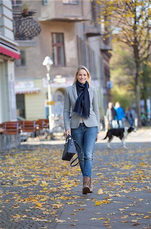 simsearch:6108-08943497,k - Pretty elegant woman walking with handbag in citycenter and smiling at camera Stock Photo - Premium Royalty-Free, Code: 6108-08943499