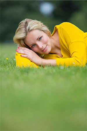 Portrait of a pretty blond woman lying down in the park smiling at camera Stock Photo - Premium Royalty-Free, Code: 6108-08943407