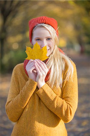 Portrait of a pretty blonde woman in park in autumn with leaf covering partially her face Stock Photo - Premium Royalty-Free, Code: 6108-08943510