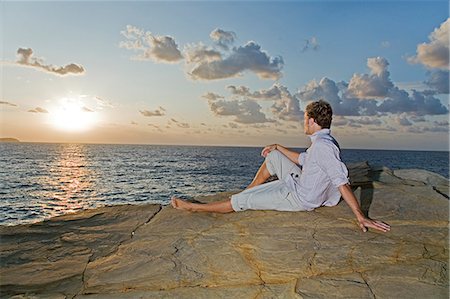 Back view of a man looking at the sunset in a cliff by the sea Stock Photo - Premium Royalty-Free, Code: 6108-08908829