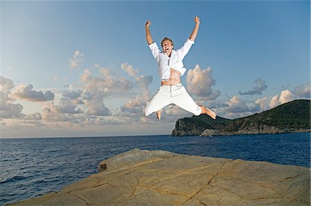 Portrait of a man jumping for joy in a cliff by the sea Stock Photo - Premium Royalty-Free, Code: 6108-08908831