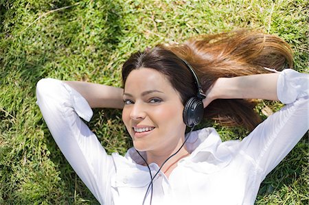 simsearch:400-07833284,k - Brunette woman lying on the grass in the park smiling at camera and listening to music Stock Photo - Premium Royalty-Free, Code: 6108-08909130