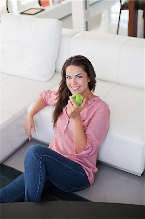 summer eating and clothes - Pretty brunette woman eating apple in living room Stock Photo - Premium Royalty-Free, Code: 6108-08909490