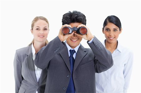 simsearch:6109-06002847,k - Smiling businessman looking through binoculars with two women behind him against white background Foto de stock - Royalty Free Premium, Número: 6109-06002863