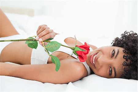 simsearch:6109-06002938,k - Portrait d'une femme aux cheveux crépuse souriante, allongée sur son lit avec une rose dans une salle lumineuse Photographie de stock - Premium Libres de Droits, Code: 6109-06002922