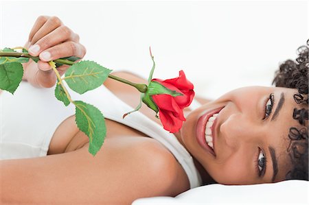 simsearch:6109-06002938,k - Portrait d'une jolie femme aux cheveux crépuse, allongée sur son lit avec une rose dans une salle lumineuse Photographie de stock - Premium Libres de Droits, Code: 6109-06002924