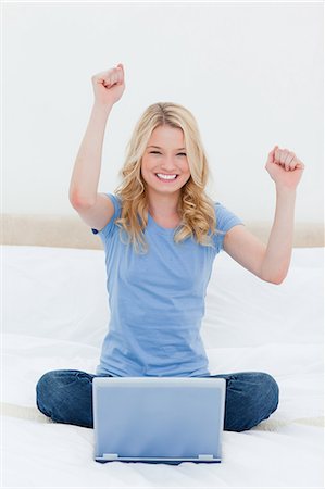 A woman is looking forward with a smile as she celebrates on the bed in front of her laptop. Stock Photo - Premium Royalty-Free, Code: 6109-06003092