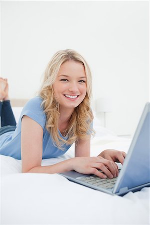 A woman looking forward with her laptop as she smiles. while lying on her bed. Stock Photo - Premium Royalty-Free, Code: 6109-06003022