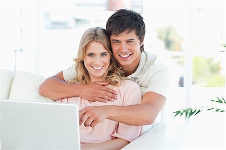 A man holds a woman as they use the laptop together and look in front of them. Stock Photo - Premium Royalty-Free, Code: 6109-06003166