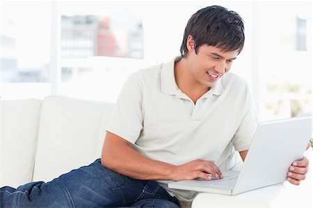 A man sitting on the couch with his laptop on the table and smiling. Stock Photo - Premium Royalty-Free, Code: 6109-06003179