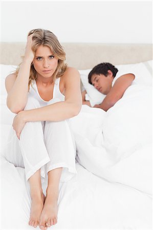 Une femme inquiète est assis sur le lit regardant vers l'avant comme l'homme dort dans son lit. Photographie de stock - Premium Libres de Droits, Code: 6109-06003243