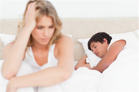 sleeping romance pic - Focus shot on the sleeping man as the woman worries at the end of the bed. Stock Photo - Premium Royalty-Free, Code: 6109-06003244