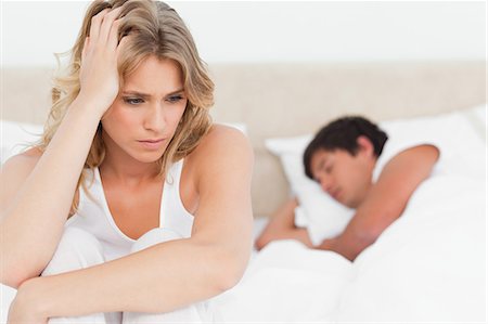 relationship distraught - The man sleeps in the bed while the focus is on the woman worrying at the edge of the bed. Stock Photo - Premium Royalty-Free, Code: 6109-06003245