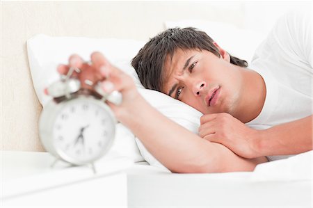 Focus on the man silencing his alarm clock with his hand as he lies in bed. Stock Photo - Premium Royalty-Free, Code: 6109-06003289