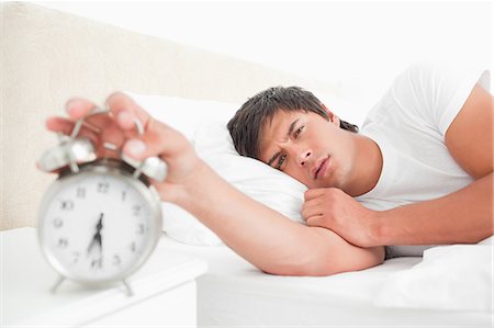 A man turning off his alarm clock with his hand looking straight ahead. Stock Photo - Premium Royalty-Free, Code: 6109-06003293