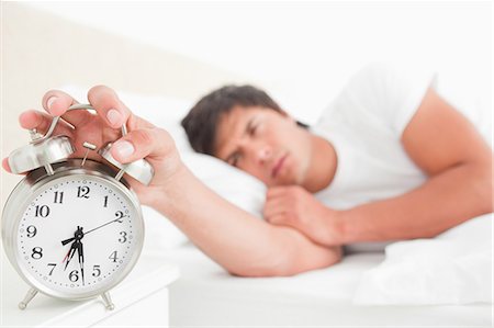 Close up and focus on the alarm clock which the half awake man is turning off with his hand. Foto de stock - Sin royalties Premium, Código: 6109-06003291