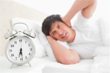 Focus on the alarm clock as it rings loudly making the man block his ears. Stock Photo - Premium Royalty-Free, Code: 6109-06003295