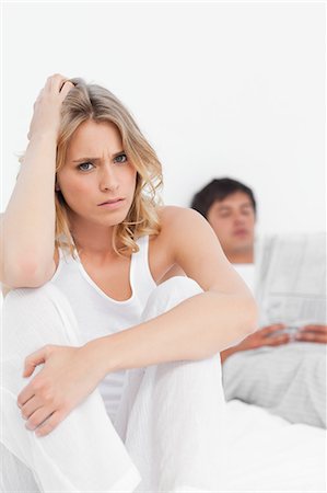 people upset not senior not child - A close up shot of a woman sitting at the edge of the bed looking worried as the man sits back reading the paper. Stock Photo - Premium Royalty-Free, Code: 6109-06003237