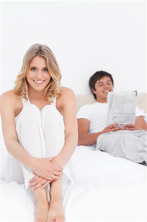 simsearch:6109-06003220,k - Une femme assise sur le lit en souriant comme l'homme est assis sur l'autre extrémité, la lecture de son journal. Photographie de stock - Premium Libres de Droits, Code: 6109-06003234