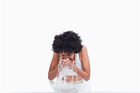 Young woman rinsing her face in front of a bowl of water Stock Photo - Premium Royalty-Free, Code: 6109-06003357