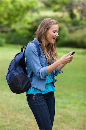 students laughing - Young happy girl carrying a backpack while receiving a text on her mobile phone Stock Photo - Premium Royalty-Free, Code: 6109-06003391