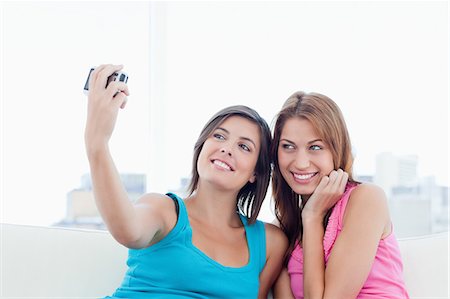 Two smiling teenagers photographing themselves while sitting on a white sofa Stock Photo - Premium Royalty-Free, Code: 6109-06003303