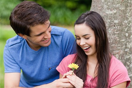 Young man giving a flower to his girlfriend while leaning against a tree Stock Photo - Premium Royalty-Free, Code: 6109-06003457