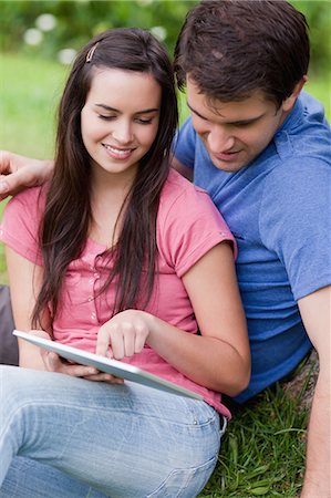 Young lovely couple sitting in a parkland while looking at a tablet computer Stock Photo - Premium Royalty-Free, Code: 6109-06003466