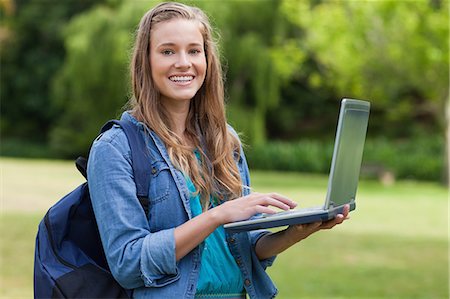 simsearch:6109-06003402,k - Young happy girl using her laptop while carrying her backpack and standing in a park Foto de stock - Sin royalties Premium, Código: 6109-06003410