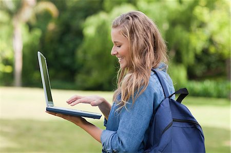simsearch:6109-06003402,k - Young happy girl standing in a park while holding a laptop and carrying a backpack Foto de stock - Sin royalties Premium, Código: 6109-06003412
