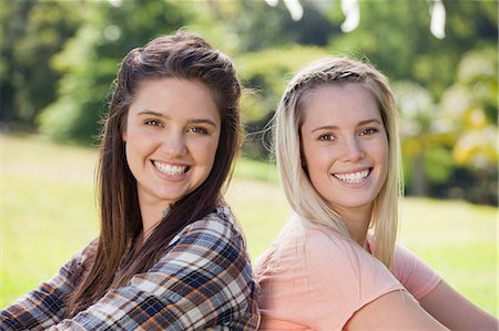 Young smiling girls standing back to back in a park while looking at the camera Stock Photo - Premium Royalty-Free, Code: 6109-06003541