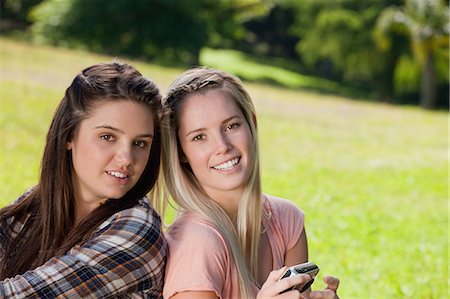 Smiling teenager holding a camera while standing up with her friend in a park Stock Photo - Premium Royalty-Free, Code: 6109-06003549