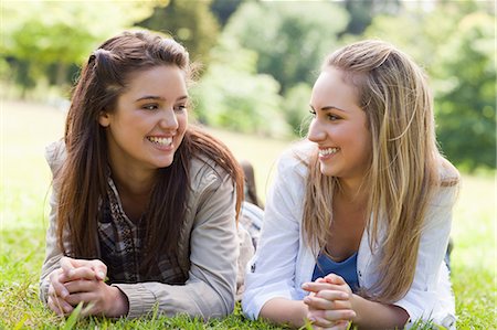 simsearch:6109-06003537,k - Two young smiling girls looking at each other while lying on the grass in a parkland Fotografie stock - Premium Royalty-Free, Codice: 6109-06003500