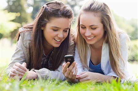 simsearch:6109-06003526,k - Two smiling friends lying on the grass in a park while looking at a text on a cellphone Stock Photo - Premium Royalty-Free, Code: 6109-06003502