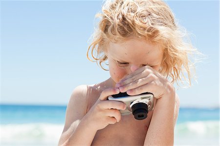 Petit garçon en regardant l'écran de la caméra à la plage Photographie de stock - Premium Libres de Droits, Code: 6109-06003771