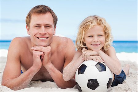 football father and sons - Happy father and son lying on the beach with football Stock Photo - Premium Royalty-Free, Code: 6109-06003734