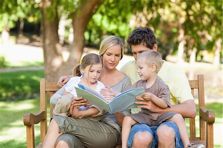 simsearch:6109-06003980,k - A smiling family enjoying a book while they sit on the park bench Foto de stock - Sin royalties Premium, Código: 6109-06004049